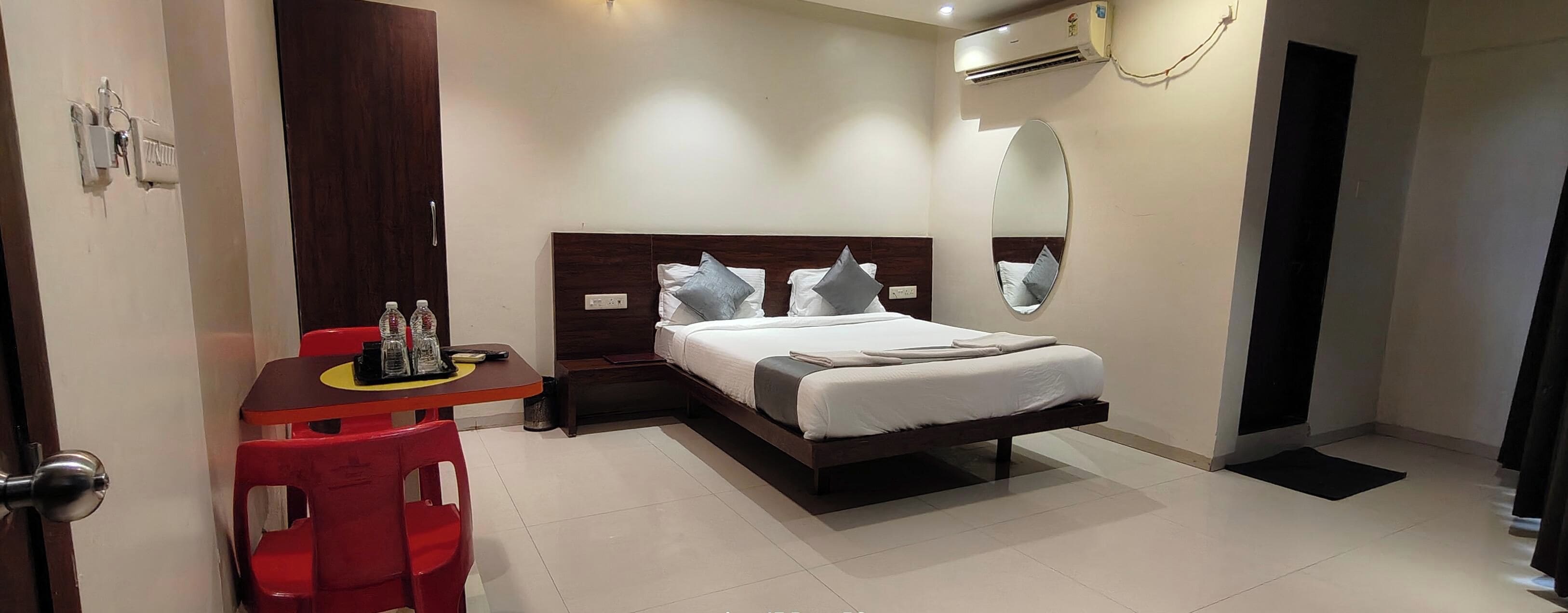 A hotel room with a bed, bedside table, and a red chair.