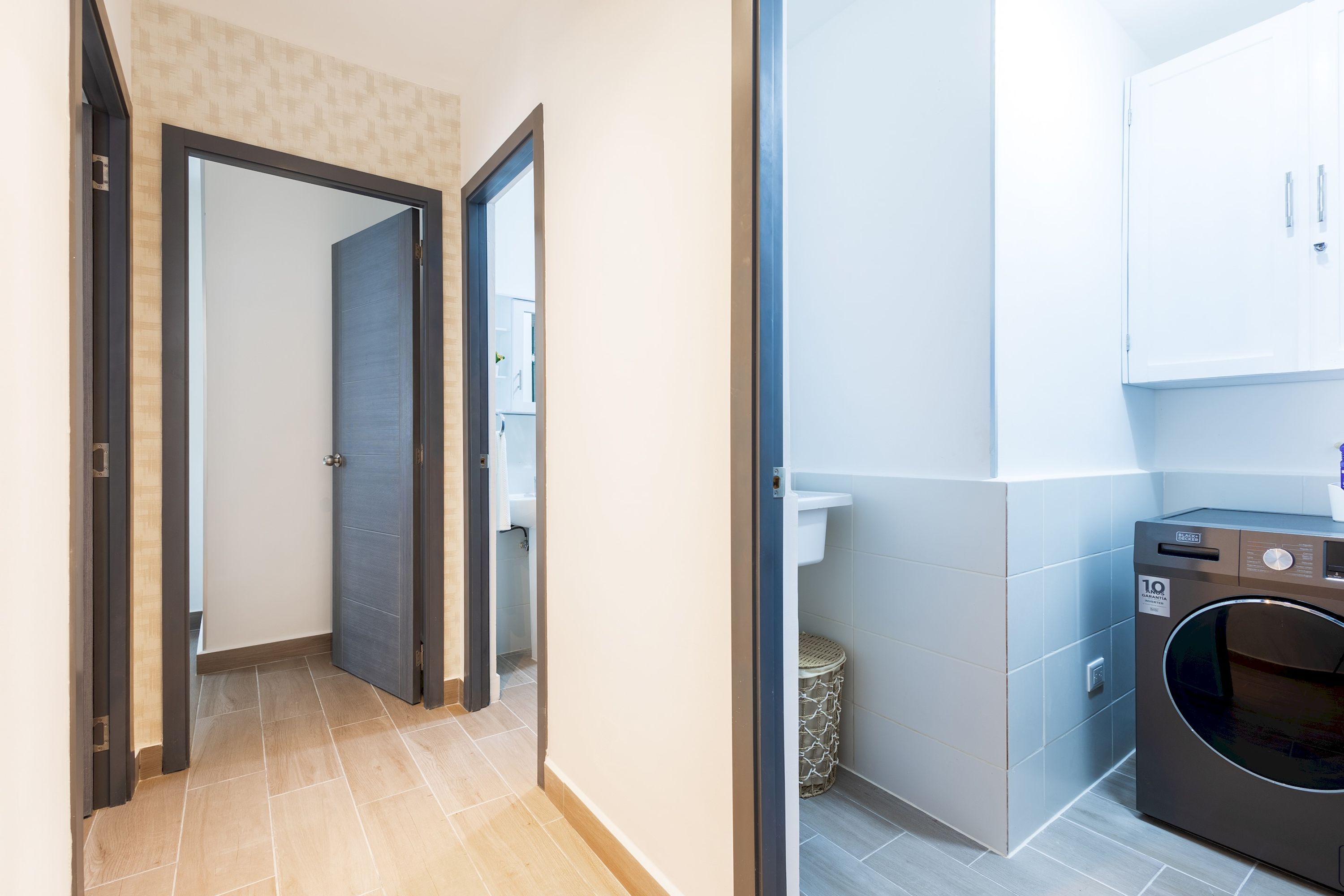 A hallway leading to a room with a door, a laundry area with a washing machine, and a trash bin.