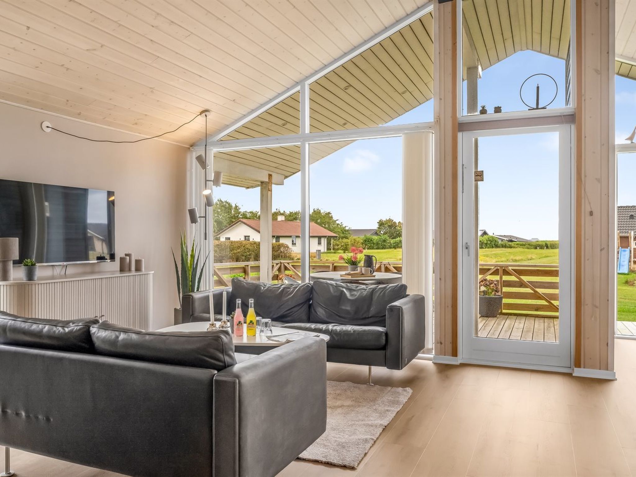 A modern living room with a large TV, leather sofas, and a glass door leading to an outdoor deck.