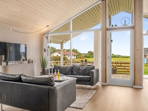 A modern living room with a large TV, leather sofas, and a glass door leading to an outdoor deck. - "Clarice" - 250m to the fjord by Interhome (Vinderup)