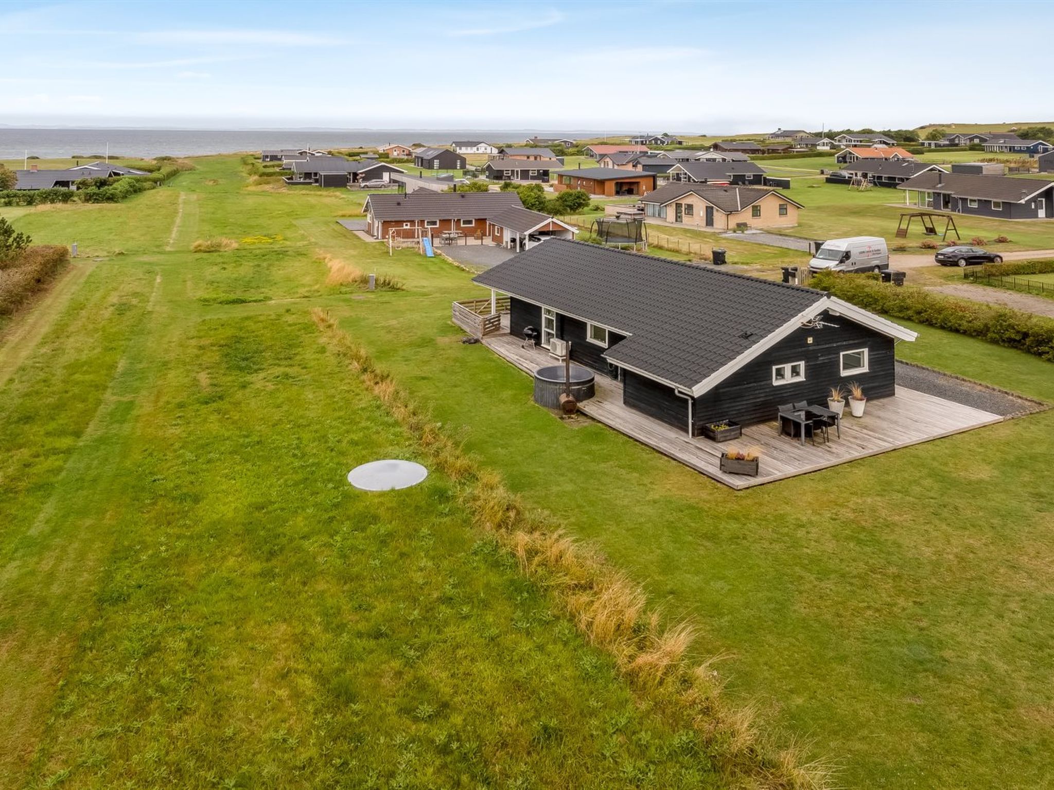 A residential area with houses, a grassy field, and a body of water in the background.