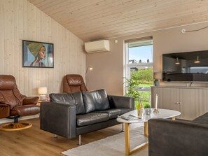 En moderne stue med en sort lædersofa, en brun læderstol, et lille rundt bord og et fjernsyn.