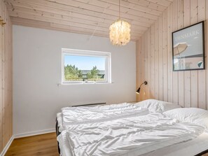 Et soveværelse med seng, et vindue, en væglampe og et billede i ramme.