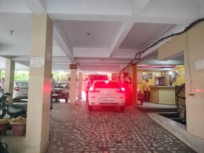 A covered parking area with a white car parked in the center, a motorcycle to the left, and a building entrance to the right. - Classic RIO Patna (Patna)