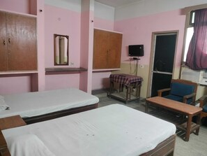 A room with two beds, a wooden wardrobe, a small table with a checkered tablecloth, a television mounted on the wall, and a window with curtains. - Classic RIO Patna (Patna)