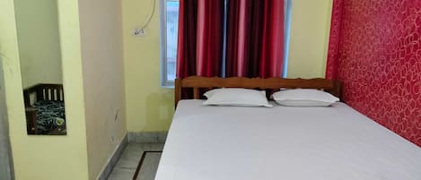 A bedroom with a bed, a window with curtains, an air conditioning unit, and a mirror.