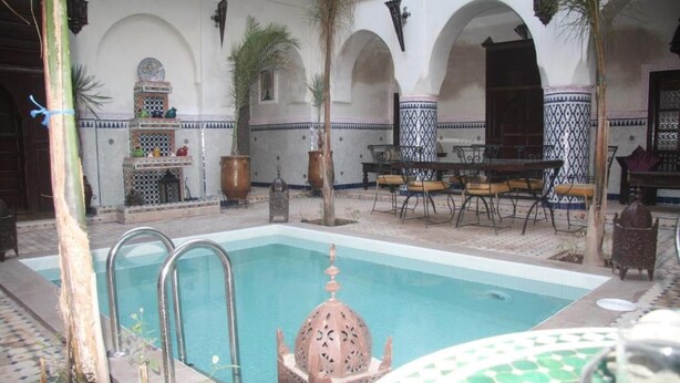 Piscina com uma fonte decorativa, rodeada por um pátio com mesas e cadeiras.