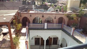 Um pátio com um edifício branco, janelas em arco e guarda-corrimão azul.