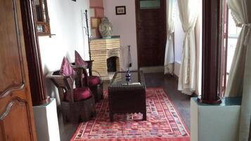 A traditional room with a wooden floor, a glass-top coffee table, a patterned rug, and a wooden cabinet with a vase.