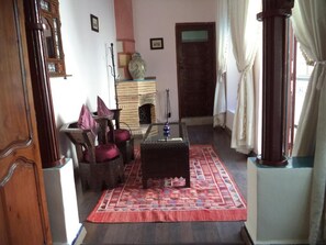 A traditional room with a wooden floor, a glass-top coffee table, a patterned rug, and a wooden cabinet with a vase. - Dar moulay Ali (Marrakech)