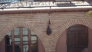 Fachada de edifício com janelas em arco e uma porta, um portão de metal decorativo e um muro com padrão.