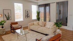 Een woonkamer met een bank, fauteuils, een glazen salontafel en een plafondventilator.