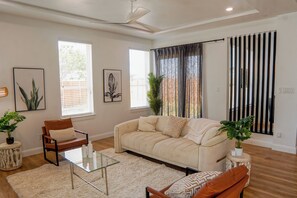 Una sala de estar con sofá, sillones, una mesa de centro de vidrio y un ventilador de techo.