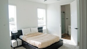 Een slaapkamer met een bed, nachtkastjes, een plafondventilator en een zichtbare badkamer door een open deur.