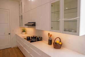 Una cocina con armarios blancos, horno empotrado y encimera con ollas, cesta de limones y utensilios de madera.