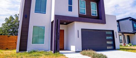 A modern two-story house with a garage, large windows, and a flat roof.