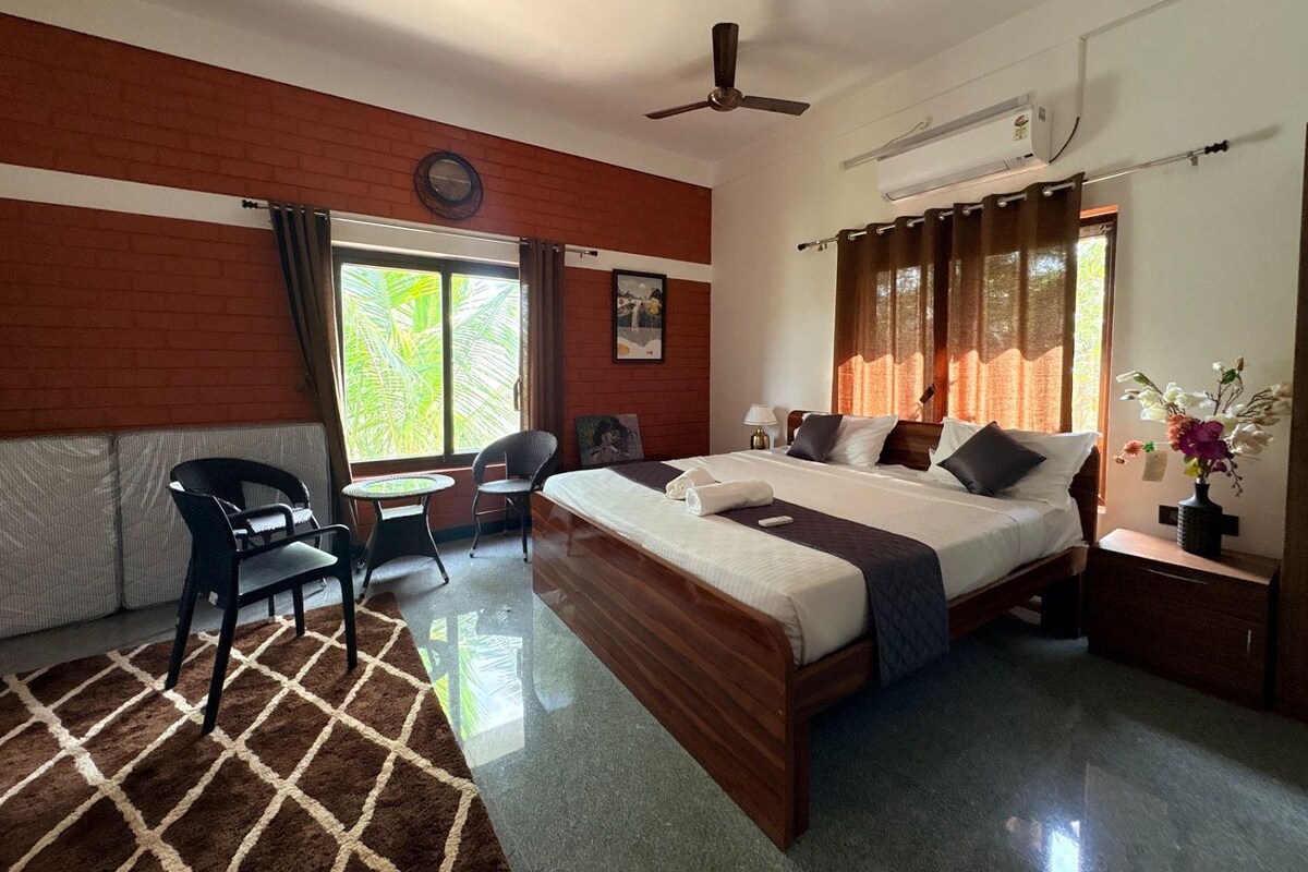 A hotel room with a bed, two chairs, a small table, a ceiling fan, and a window with curtains.