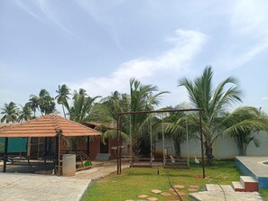 A courtyard with a swing set, palm trees, and a small building with a tiled roof.