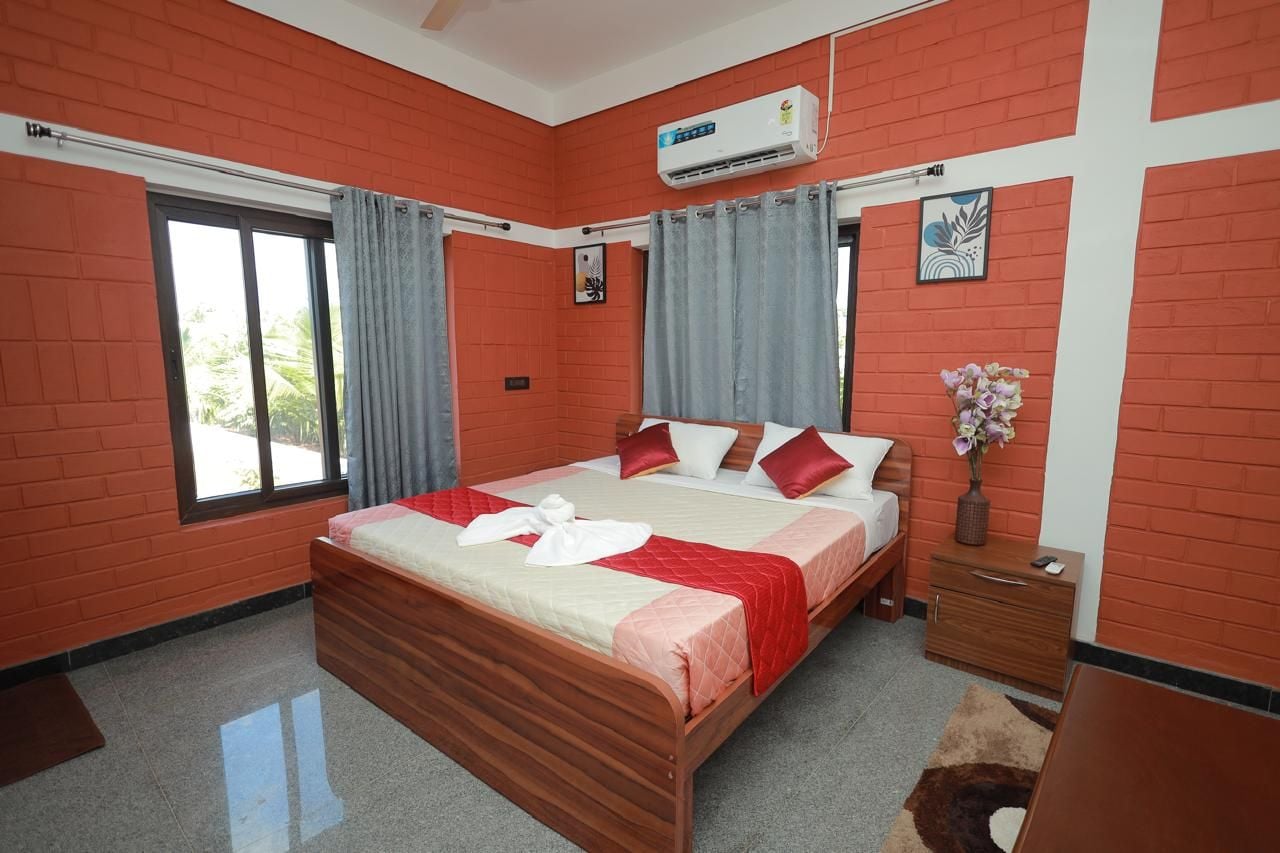 Een hotelkamer met een groot bed, een houten nachtkastje, een vaas met bloemen en een raam met gordijnen.