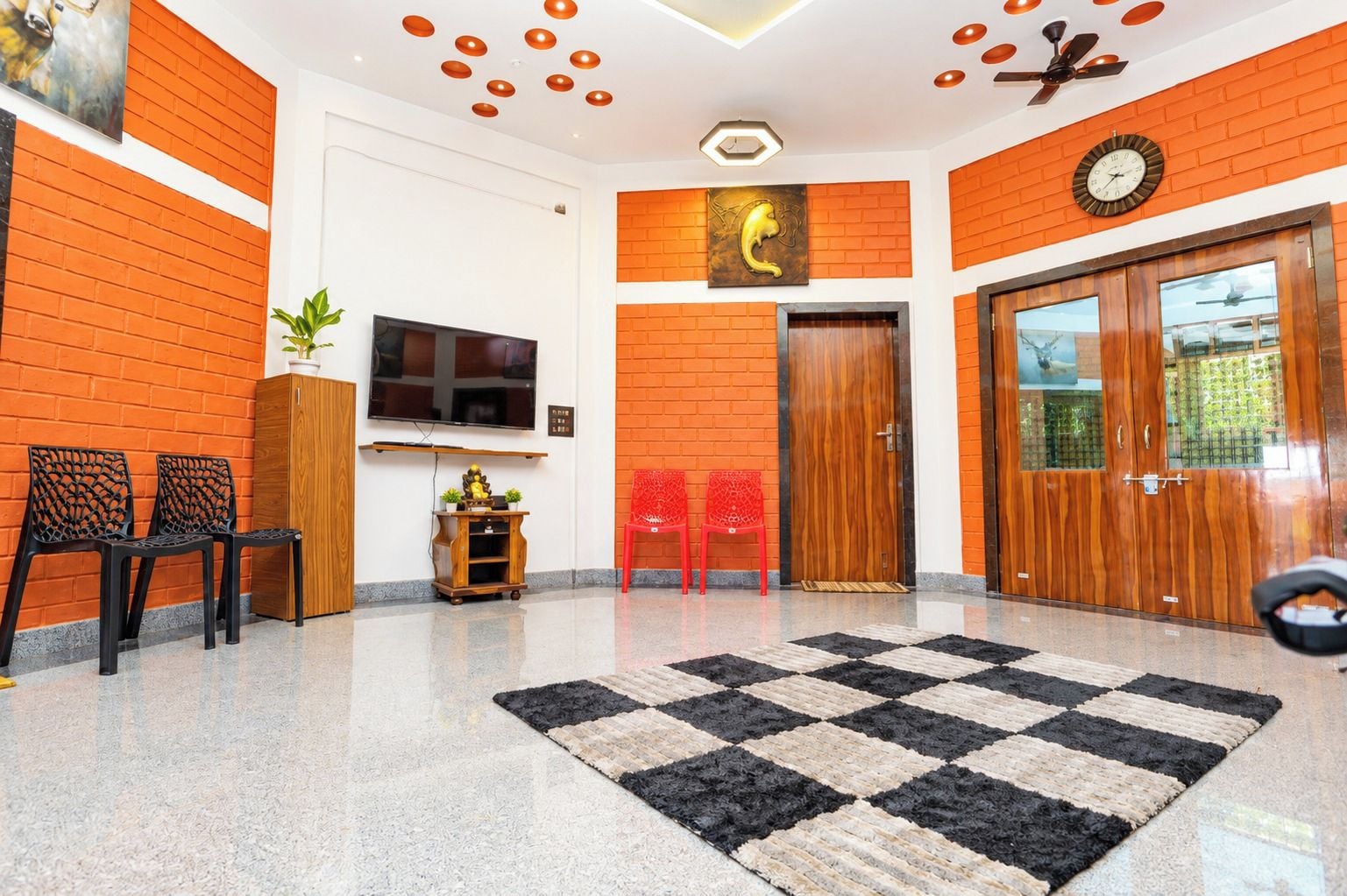 Un hall con alfombra a cuadros, un televisor, un mueble de madera y una puerta con un reloj.