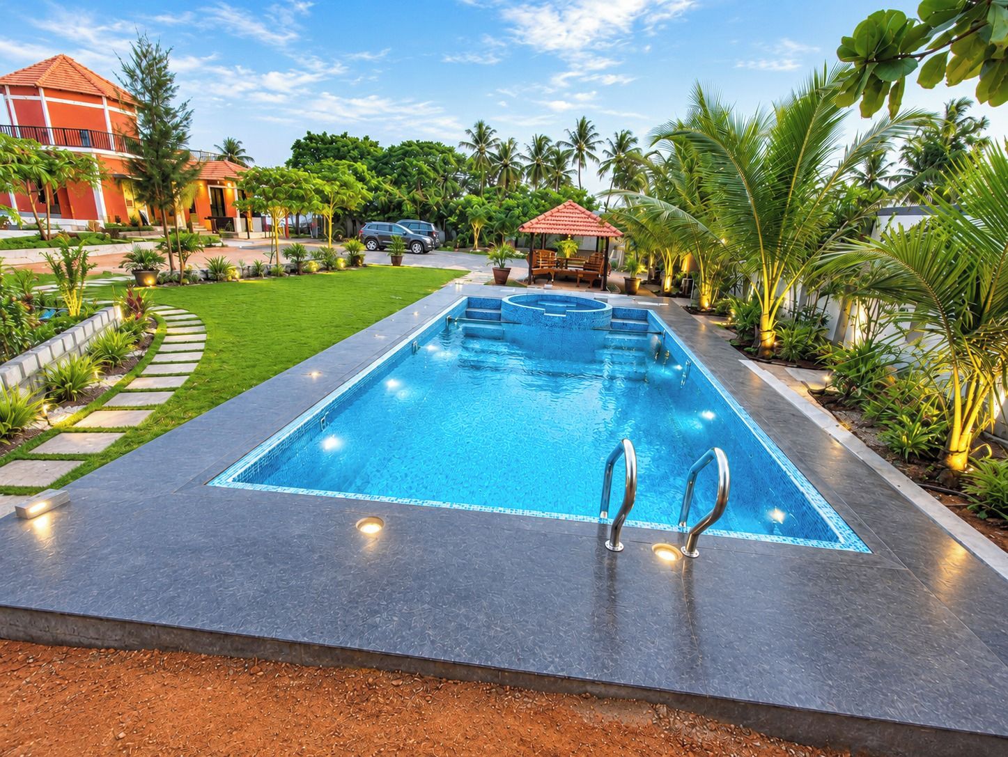 A rectangular swimming pool with a tiled edge, surrounded by a landscaped garden with palm trees and a small gazebo.