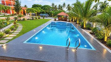 A rectangular swimming pool with a tiled edge, surrounded by a landscaped garden with palm trees and a small gazebo.