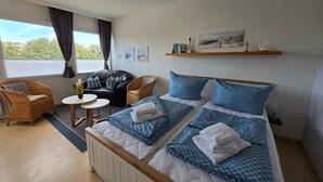 Quarto de hotel com cama, duas cadeiras, uma mesa pequena e janela com cortinas.