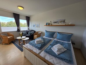 Une chambre d’hôtel avec un lit, deux chaises, une petite table et une fenêtre avec des rideaux.