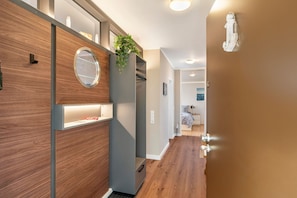 Ein moderner Flur mit Holzboden, einem integrierten Spiegel, einer Pflanze und Blick in ein Schlafzimmer mit Bett und Nachttisch.