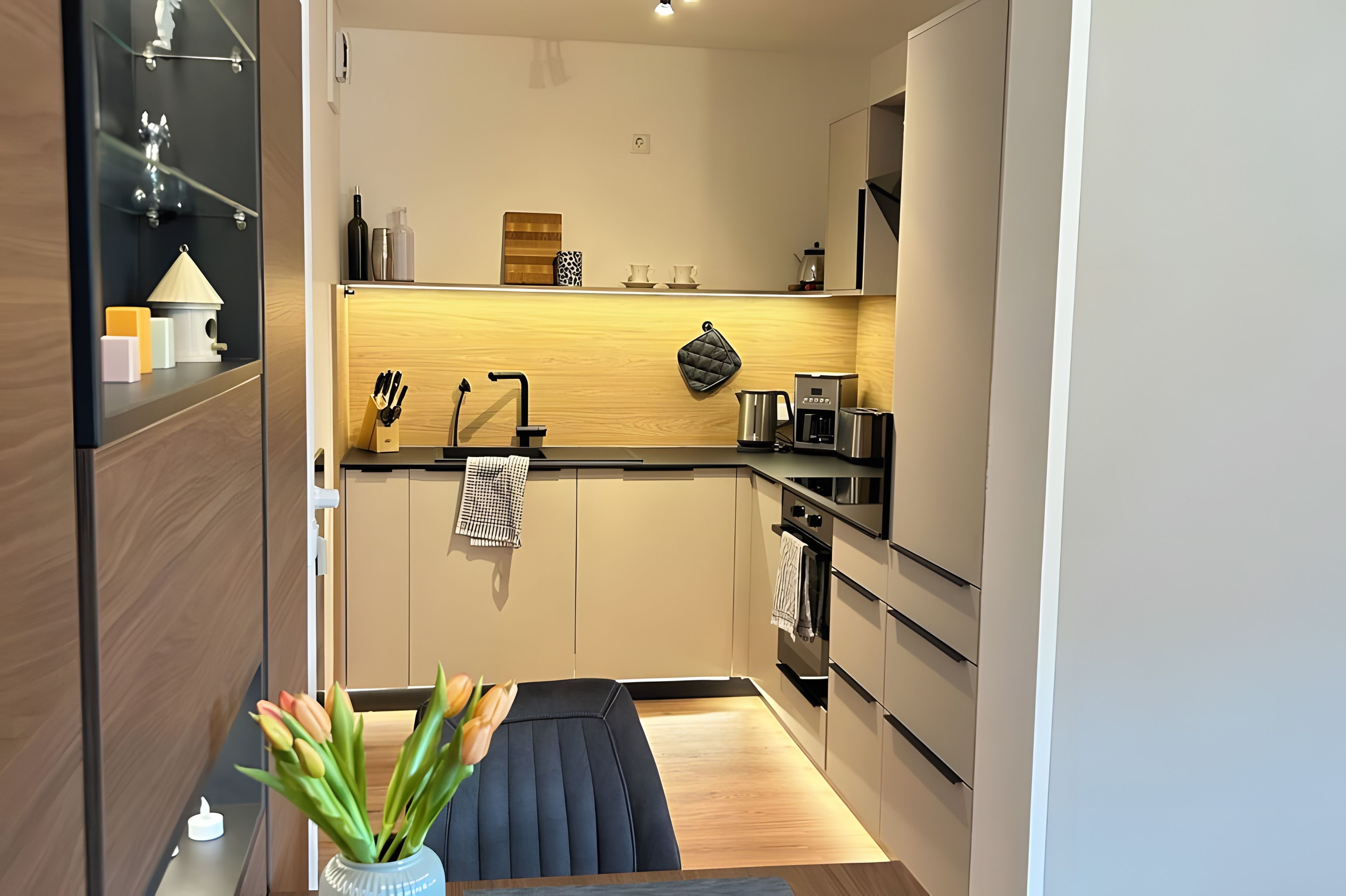 Een compacte keuken met een modern design, met een inbouwoven, een koffieapparaat en een waterkoker op het aanrecht.