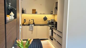 Een compacte keuken met een modern design, met een inbouwoven, een koffieapparaat en een waterkoker op het aanrecht.