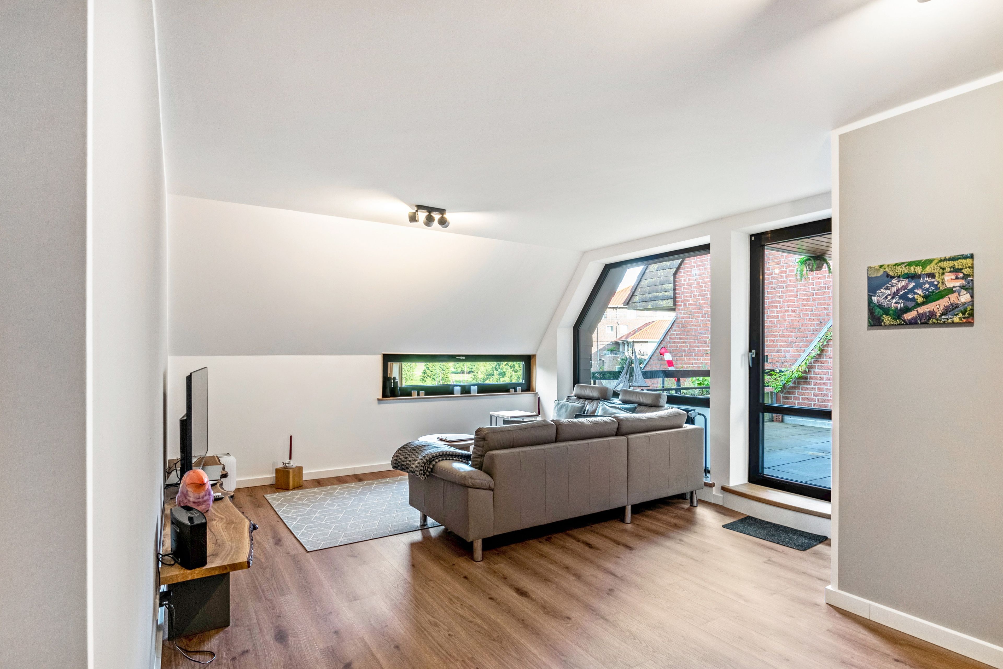 Ein moderner Loft-Wohnraum mit großem Fenster, einem grauen Sofa und Holzboden.
