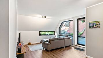 Ein moderner Loft-Wohnraum mit großem Fenster, einem grauen Sofa und Holzboden.