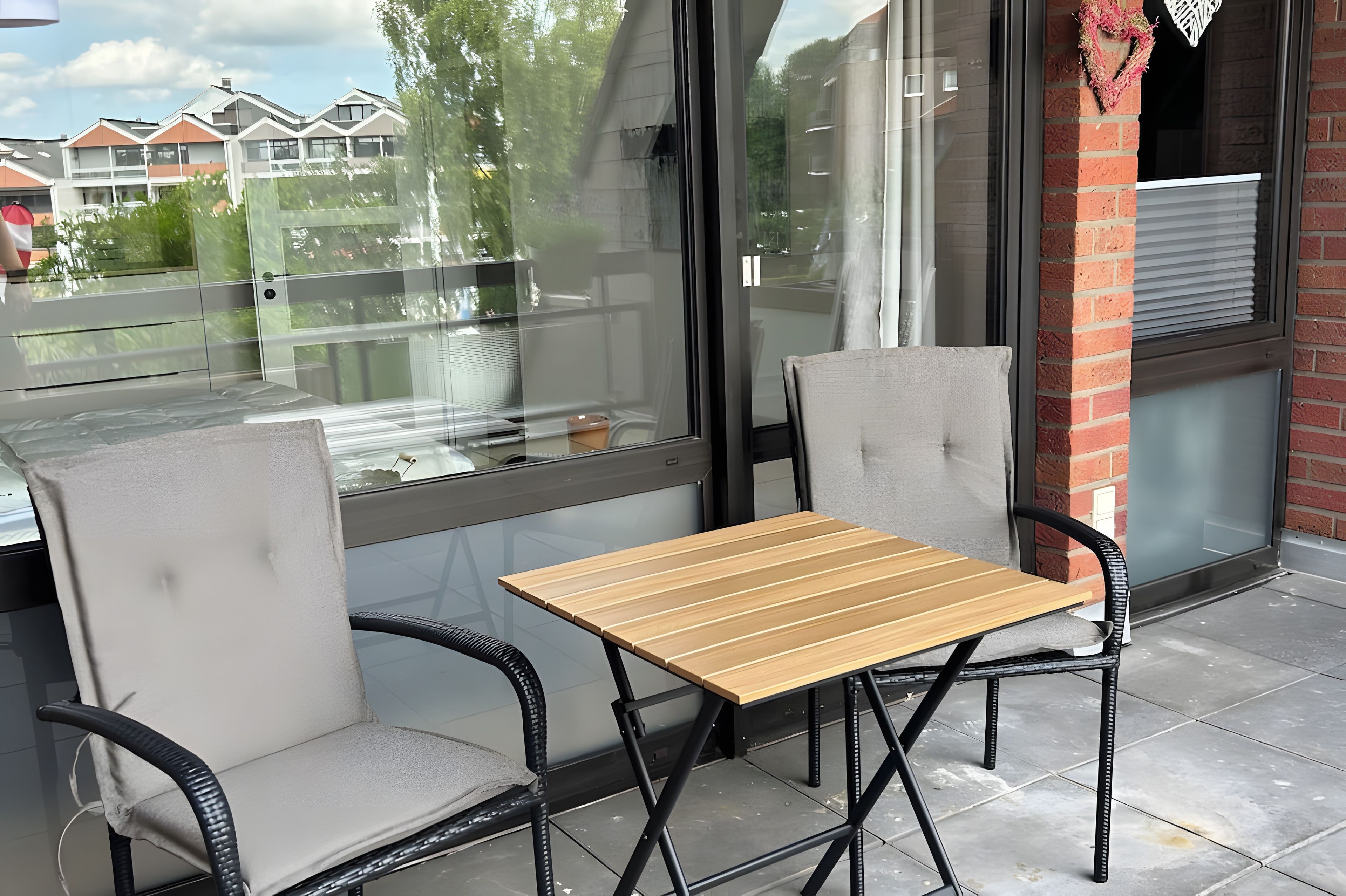 Un área de estar al aire libre con una mesa, dos sillas, una partición de vidrio y vistas a edificios al fondo.