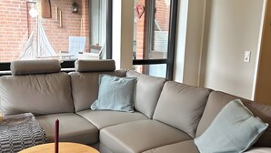 Una sala moderna con un sofá modular, una mesa redonda de madera y vistas al exterior a través de amplios ventanales.
