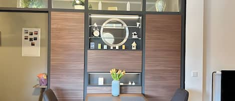 Quarto moderno com parede de painel de madeira, espelho redondo e pequena mesa com cadeiras.