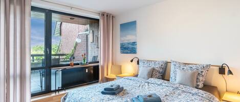 A bedroom with a large bed, a window with curtains, a desk, and a view of the outdoors.