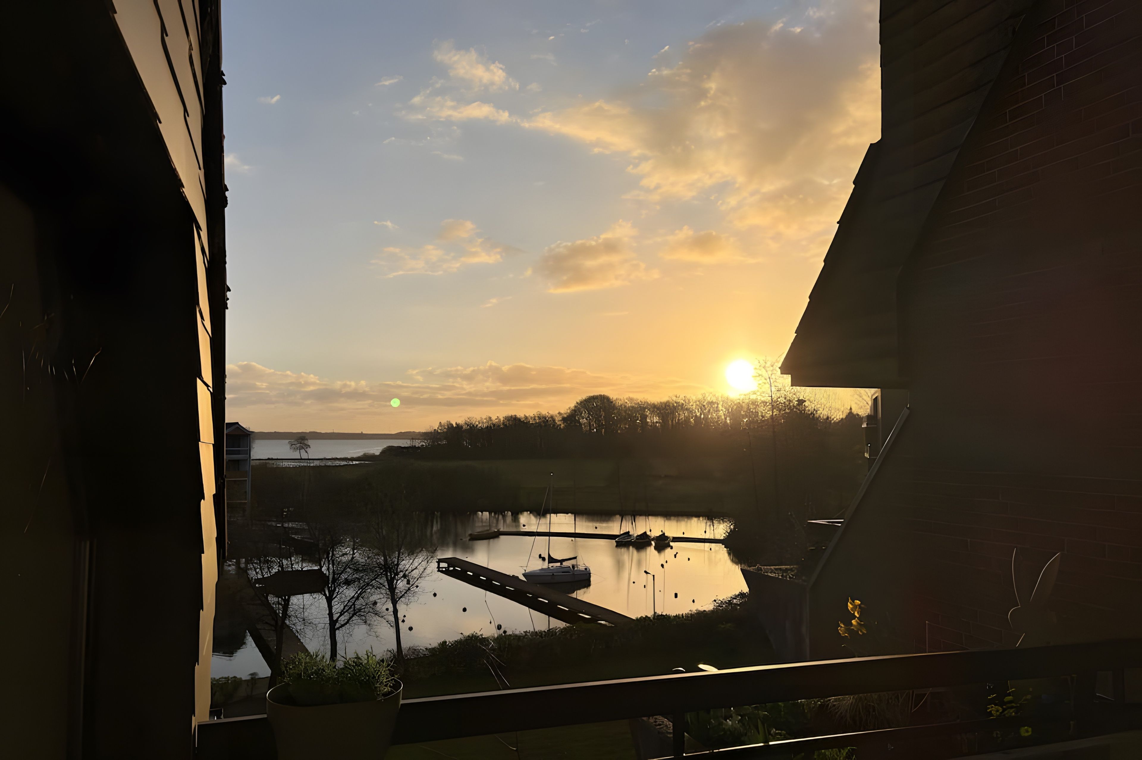 Zonsondergang vanaf een balkon met uitzicht op een wateroppervlak, boten en een verre kustlijn.