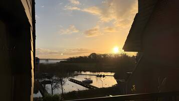 Zonsondergang vanaf een balkon met uitzicht op een wateroppervlak, boten en een verre kustlijn.