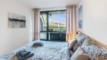 Habitación de hotel con cama, vista de edificios a través de un ventanal y un cuadro en la pared.