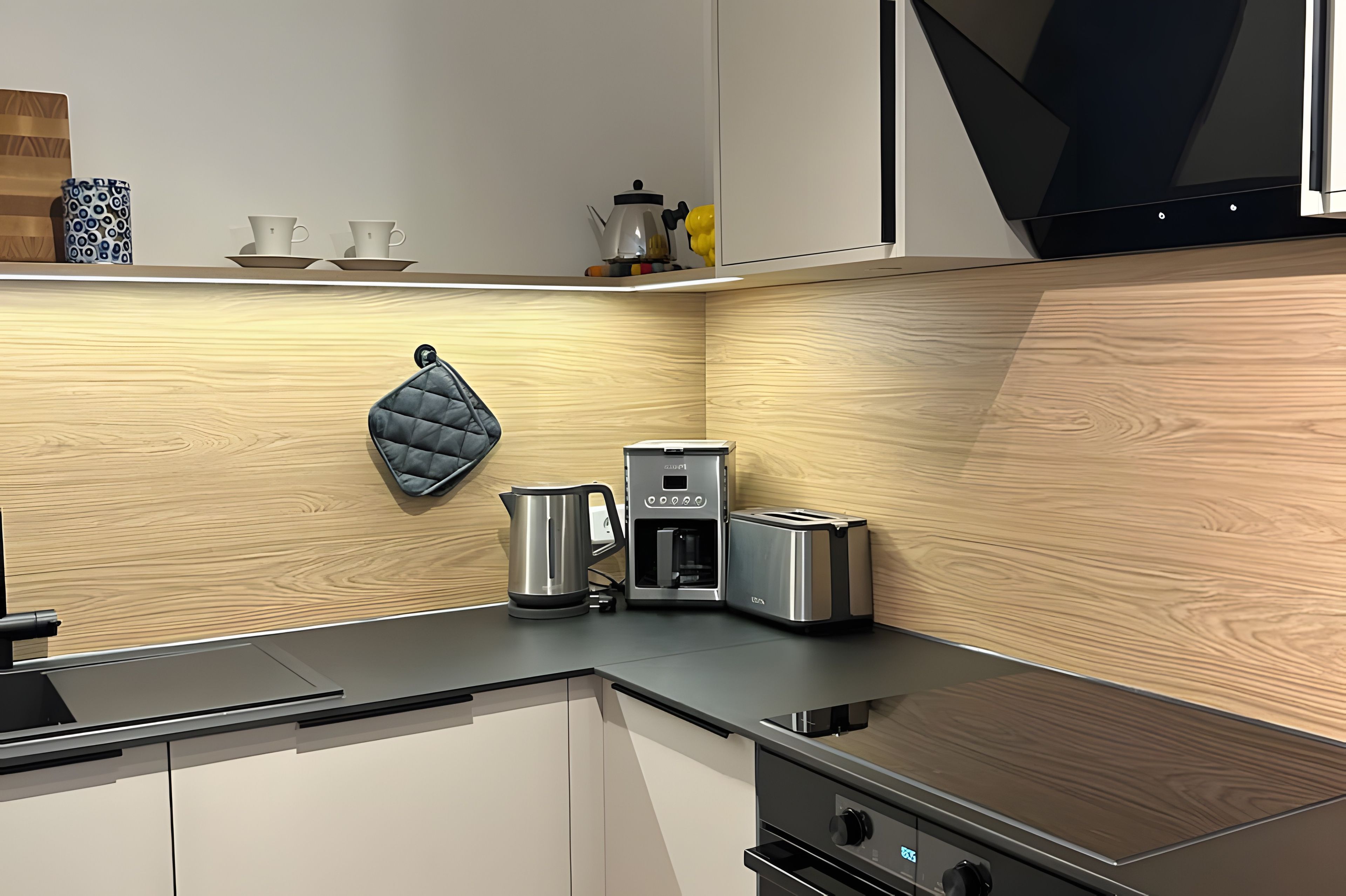 A modern kitchen with a built-in coffee maker, toaster, kettle, and a kettle hanging on the wall.