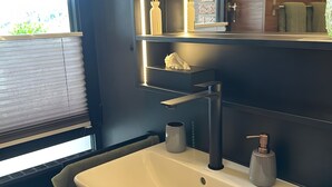 Un baño con lavamanos blanco, dispensador de toallas y una ventana con persianas.