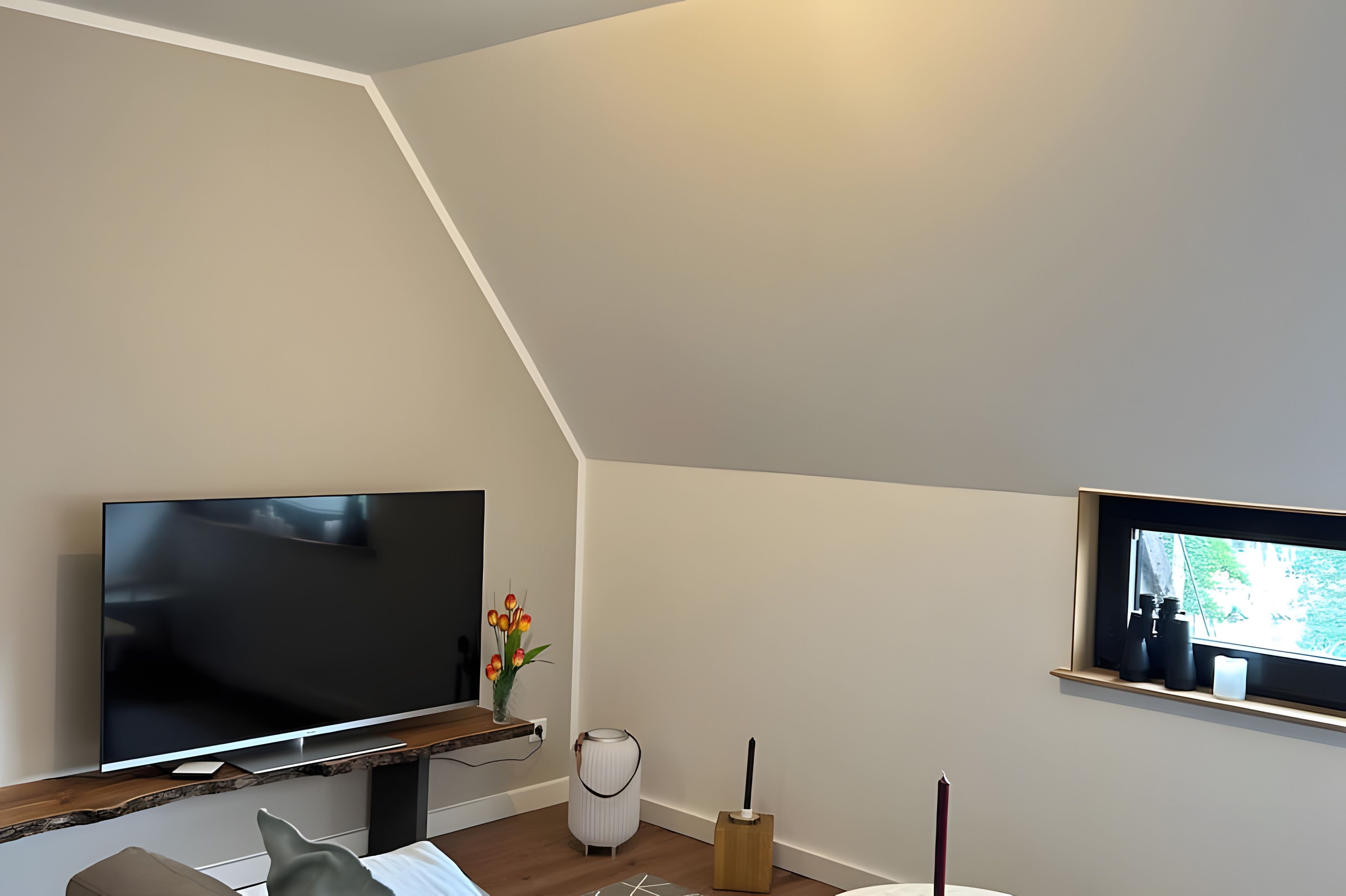 A modern living room with a flat-screen TV, a small table with a vase of flowers, and a window with binoculars.
