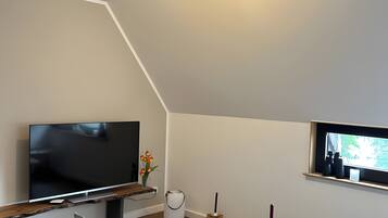 A modern living room with a flat-screen TV, a small table with a vase of flowers, and a window with binoculars.