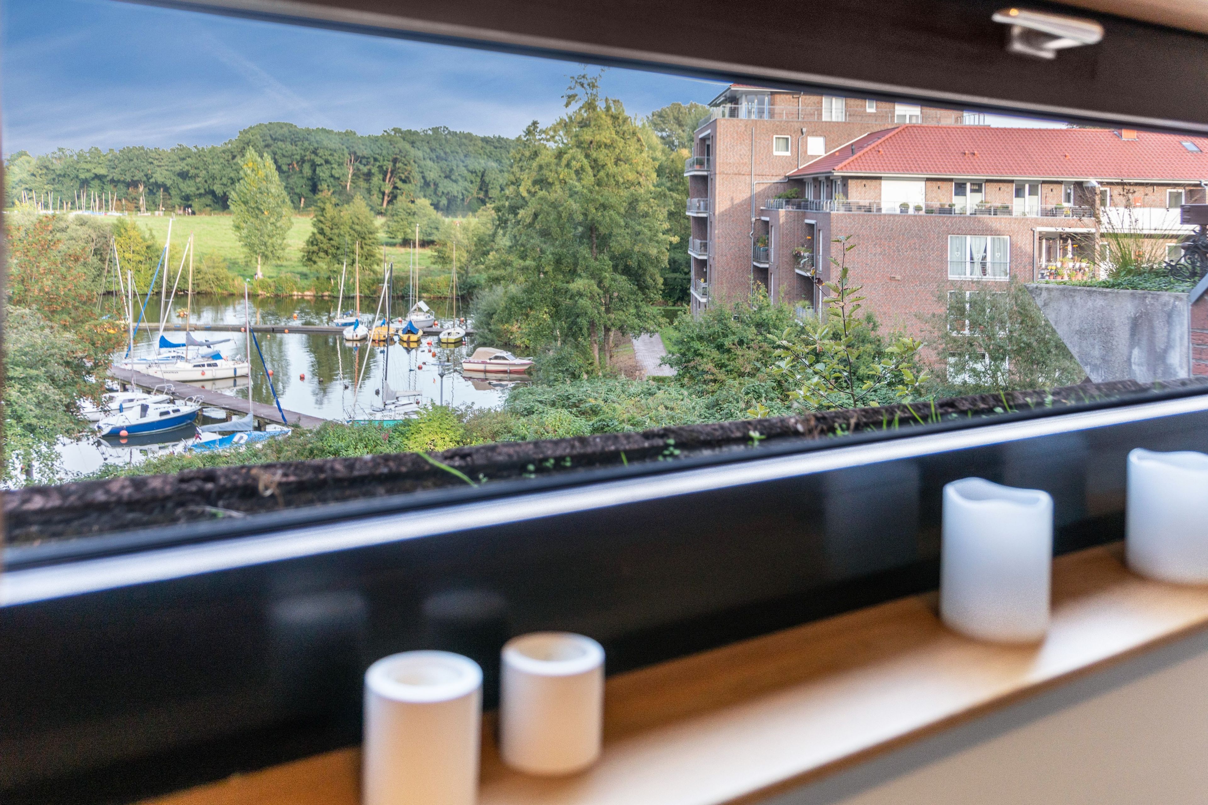 A view from a window overlooking a marina with boats, greenery, and a building in the background.