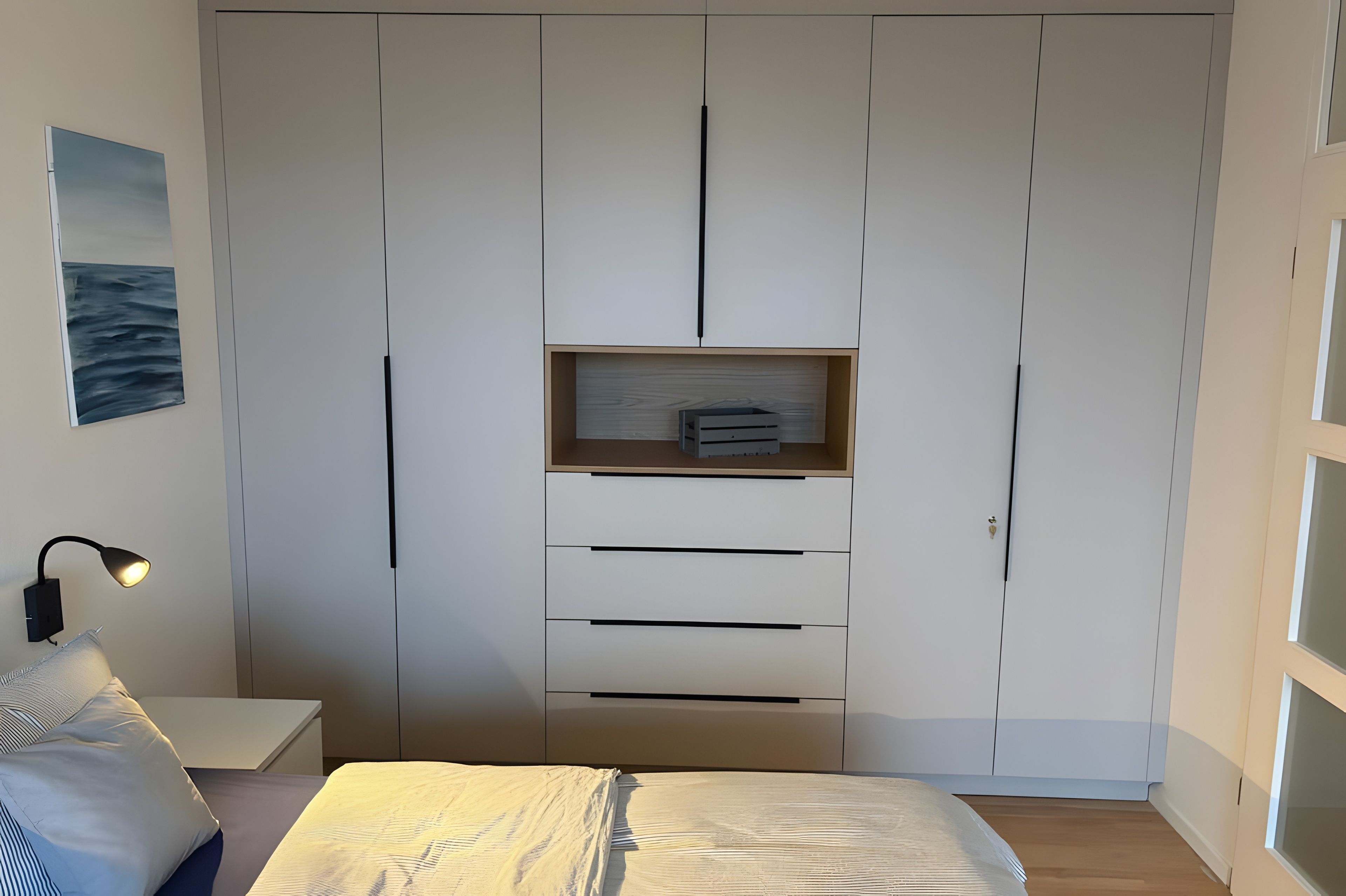 A bedroom with a bed, a bedside table, a lamp, a wardrobe, and a shelf with items.