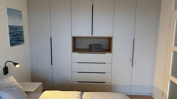 A bedroom with a bed, a bedside table, a lamp, a wardrobe, and a shelf with items.