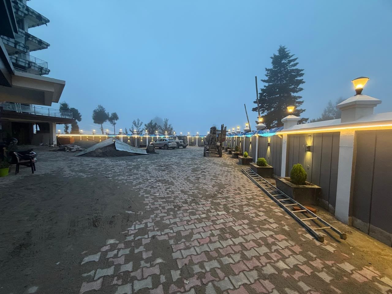 A paved pathway leading to a building with a modern design, a parked car, and a ladder.
