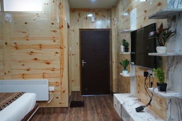 A room with wooden walls, a bed, a television, and a small plant on a shelf.