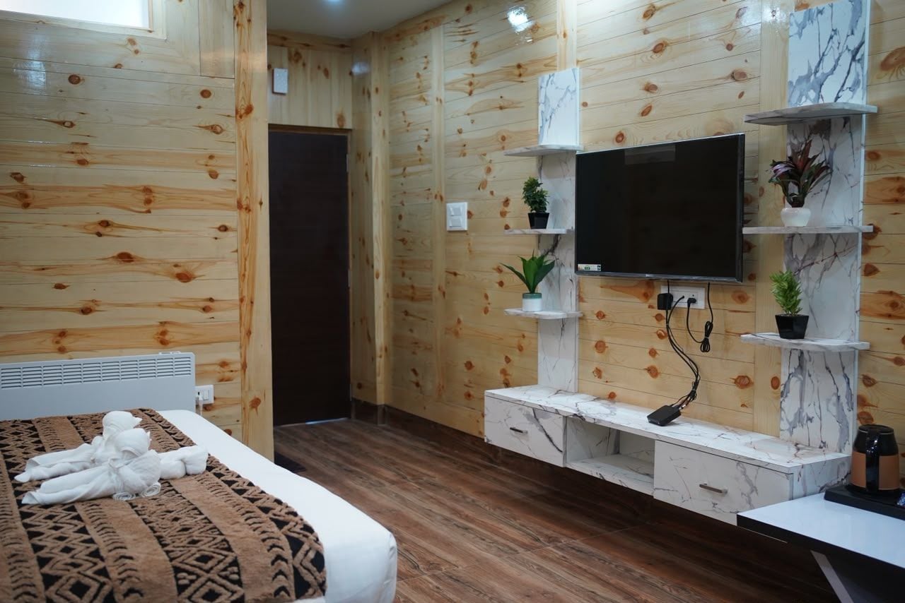 Une chambre d’hôtel avec des murs lambrissés, un lit recouvert d’une couverture à motifs, un téléviseur à écran plat fixé sur une étagère en marbre et une petite plante en pot posée sur l’étagère.